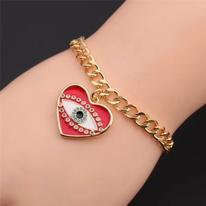 Close-up of golden chain bracelet with red enamel heart and evil eye charm on wrist