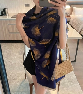 Close-up of dark blue cashmere scarf with golden ginkgo leaf pattern and fringe detail