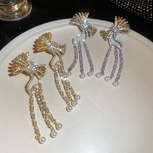 Detailed macro of gold and silver bow tassel earrings with zircon and pearl drops
