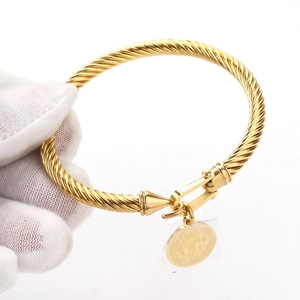 Detailed macro view of a golden twisted rope bracelet with a horseshoe buckle and medal pendant