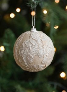 Detail of beige lace fabric wrapped Christmas ball hanging on a green tree branch