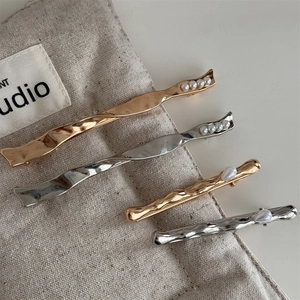 Elegant gold and silver wave hair clips with baroque pearls on a minimalist background