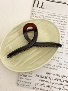 Detail of a large 13cm tortoiseshell hair claw clip with a stylish knot design on a ceramic plate