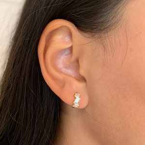 Elegant gold curved stud earrings featuring baguette cut zircons worn on model's ear