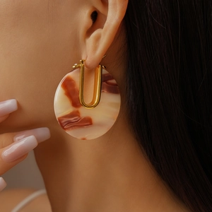 Close-up of 18k gold-plated U-shaped earrings with round tortoiseshell resin pendants