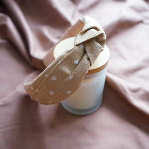 Close-up of beige woven raffia headband with white polka dot embroidery and top knot