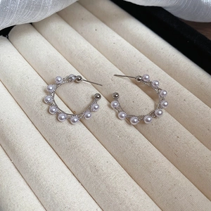 Macro detail of C-shaped silver earrings with pearls on a jewelry box background