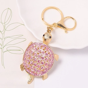 Détail d'un porte-clés tortue doré avec des strass roses posé sur une assiette blanche