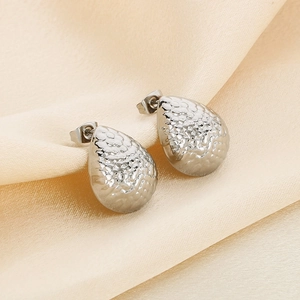 Detailed close-up of silver teardrop earrings with hammered texture on silk fabric