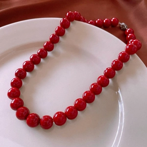 Detail of red glass beaded necklace with silver clasp on white decorative plate