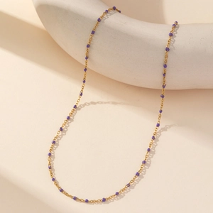 Macro detail of gold-plated chain necklace featuring purple enamel beads on curved stand