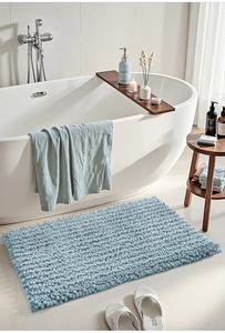 Close-up of light blue chenille bath mat with absorbent soft texture next to a bathtub
