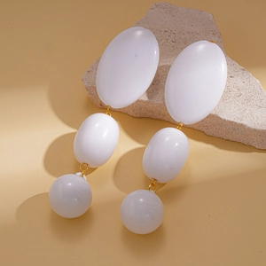 Détail de boucles d'oreilles pendantes en acrylique blanc avec anneaux dorés sur pierre