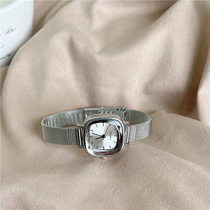 Detail of silver square dial watch with stainless steel mesh strap on beige fabric