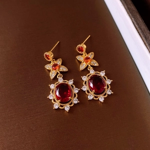 Detail of gold-plated earrings featuring oval red gemstones and sparkling crystal accents
