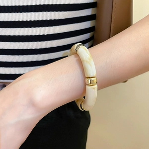 Detail view of cream resin bamboo-style bracelet with polished gold metal links on wrist