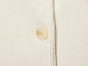 Macro shot of ivory wool coat detailing beige button and fine fabric texture