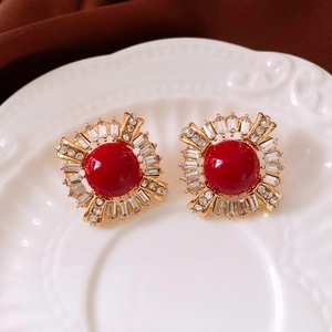 Macro detail of vintage gold earrings with red round stone and crystal halo on ceramic tray