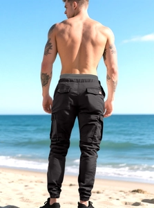 Detail of men's black multi-pocket cargo pants with grey elastic waistband on beach
