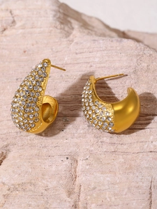 Detail of gold water-drop earrings with pavé zircons on a natural stone background