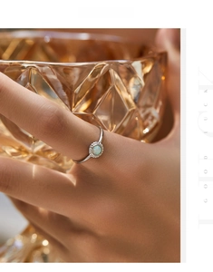 Detail of s925 silver sunflower ring with opal stone worn on finger with glass background