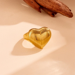Minimalist gold heart ring with striped texture on a warm neutral background