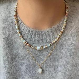 Detail of double-layer beaded necklace with freshwater pearls and gold chain on gray sweater