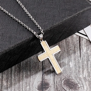Macro detail of cross pendant featuring gold frosted inlay on silver stainless steel chain