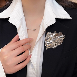 Detail of silver pleated leaf brooch and pearl heart necklace on black suit blazer