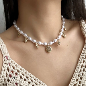 Detail of a pearl necklace with golden seashell and starfish charms on a model
