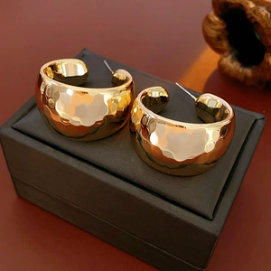 Detailed macro of golden C-shaped hoop earrings with hammered texture on jewelry box