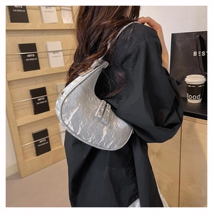 Silver metallic crescent bag with pleated texture shown on shoulder against a black shirt