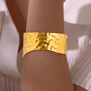 Detail of wide gold hammered texture cuff bracelet on female wrist with shiny metallic finish