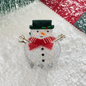 Close-up of glitter snowman hair claw clip with green hat and red bow for Christmas