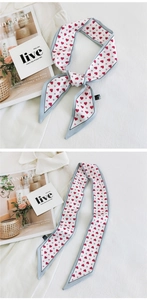 Detail of white skinny scarf with red heart pattern and blue border tied in a bow