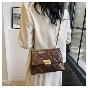 Detail of deep brown quilted crossbody bag with gold chain strap on shoulder