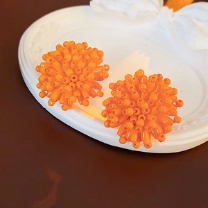 Macro shot of orange beaded flower stud earrings on a white embossed decorative tray