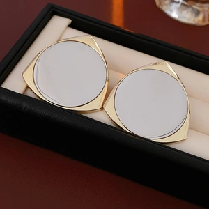 Macro shot of triangular gold and white shell earrings on a beige velvet jewelry pad