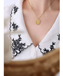 Detail of a gold oval rose engraved pendant necklace worn by a model in a white shirt
