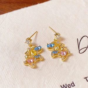Macro detail of gold rabbit stud earrings with colorful heart and teardrop gemstones