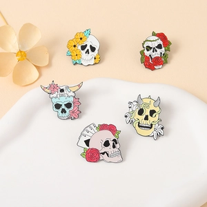 Five unique skull enamel pins with floral and card designs on a white ceramic tray