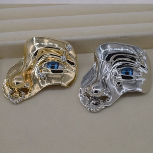 Detailed close-up of face-shaped brooches in gold and silver with blue eye and rhinestones