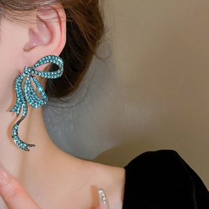 Close-up of a large silver bow earring with turquoise rhinestones worn on the ear