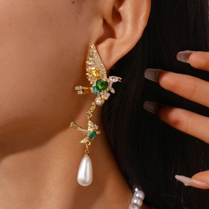 Detailed view of ornate golden bird earrings with emerald hearts and drop pearls