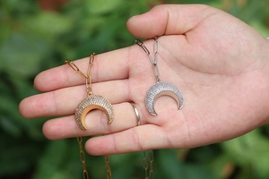 Detailed macro view of gold and silver crescent horn pendants on paperclip chains