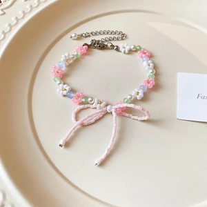 Detail of beaded flower bracelet with pink bow and silver extension chain on plate