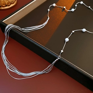 Detail of silver multi-layer tassel necklace with white pearls on a dark tray