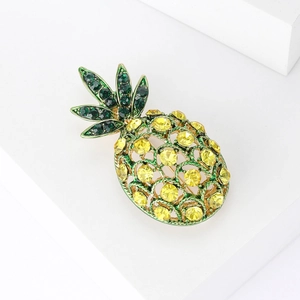 Minimalist pineapple brooch with green and yellow rhinestones on a white geometric stand