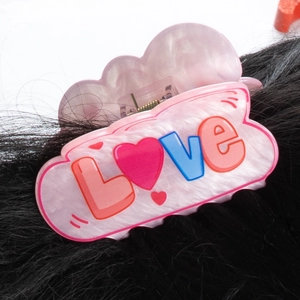 Detalle de pinza para el cabello rosa con texto LOVE y patrón de corazón en pelo negro