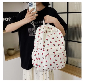 Close-up of white corduroy backpack featuring red strawberry prints and front zipper pocket